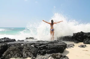 Femme courageuse affrontant une vague en bord de mer, symbolisant la force et la confiance en soi face aux défis.