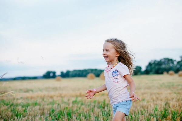 Petite fille courant joyeusement dans un champ, symbolisant la liberté et la gestion positive des émotions.